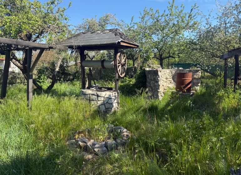 NOVINKA NA PREDAJ chata na slnečnom pozemku – Malacky - Záhrada pri chate v Malackách s kamennou studňou a divokou trávou.