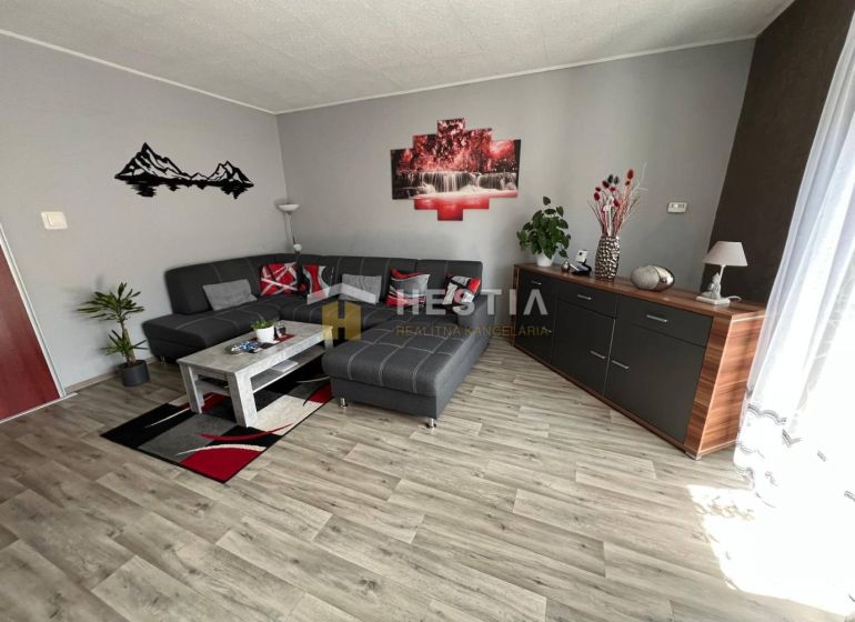 NOVINKA Priestranný 3-izbový byt (99 m²) s pozemkom, terasou, 2 balkón - Obývacia izba v 3-izbovom byte s podlahou s dreveným dekorom a šedým gaučom.