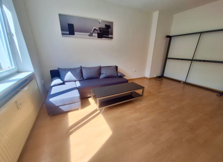 NA PRENÁJOM 1 IZBOVÝ TEHLOVÝ BYT, 34 M2, KOŠICE - ŠACA - Obývacia izba v 1-izbovom byte s gaučom a podlahou s dreveným dekorom.