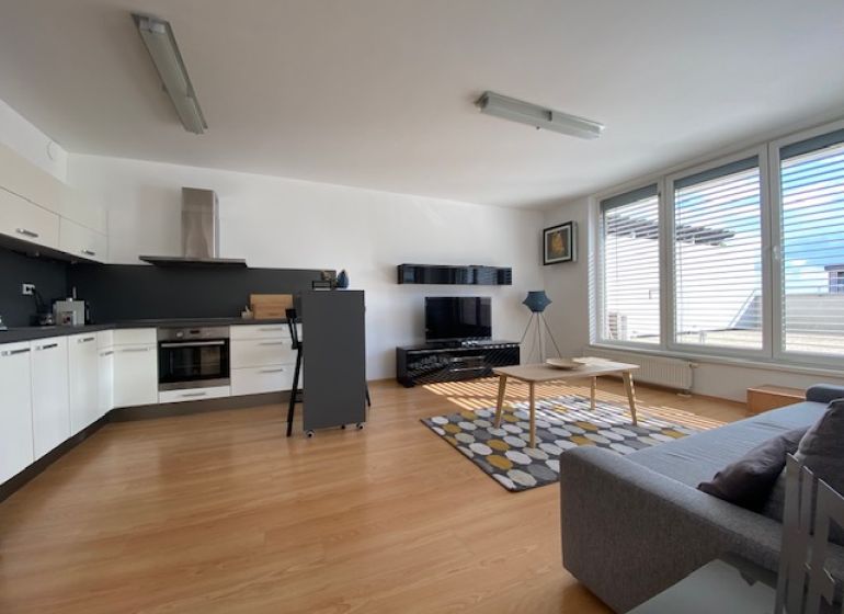 Prenájom 2 izbový 78 m2 + 30 m2 terasa,novostavba Koliba,zariadený - Obývacia izba 2-izbového bytu s podlahou s dreveným dekorom, kuchyňou a oknami.