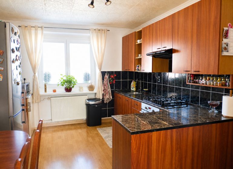 Predaj, 2 - izbový byt, Žiar nad Hronom - Kuchyňa v 2-izbovom byte s podlahou s dreveným dekorom a tmavými obkladmi.