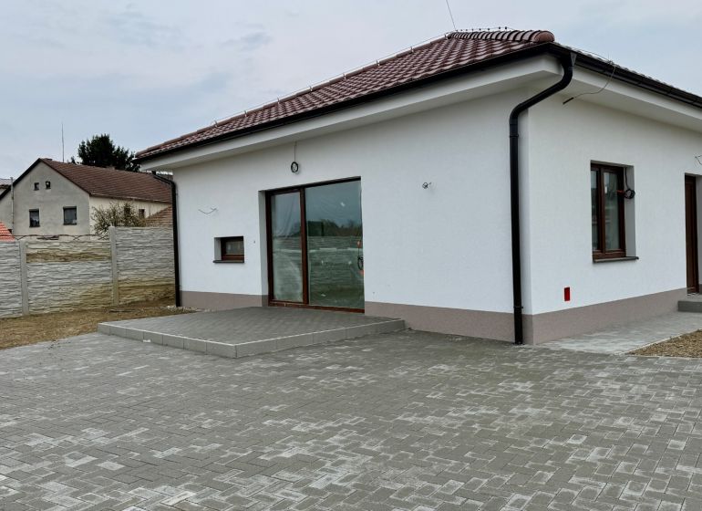 * novostavba moderného 4i domu, Vlčany, centrum - Rodinný dom na Hlavnej ulici vo Vlčanoch s bielou fasádou a dláždeným nádvorím.