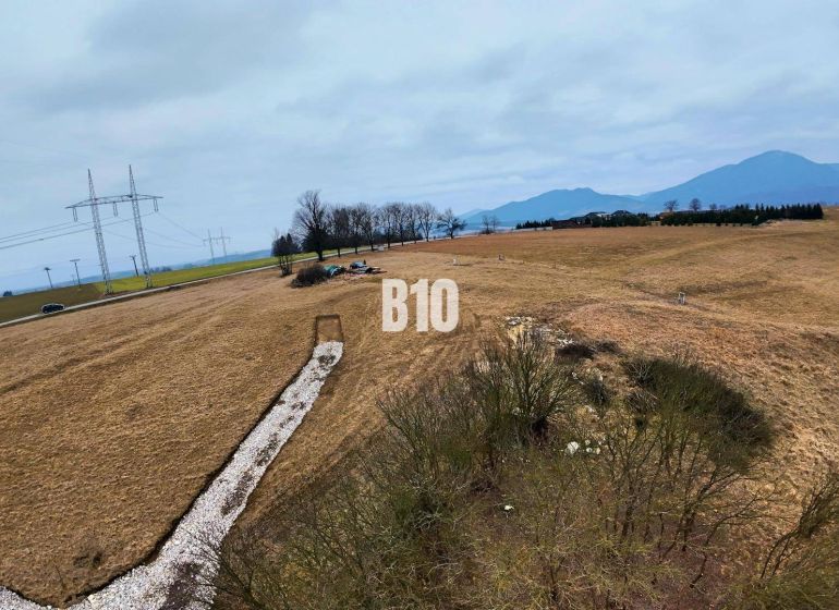 Veľký stavebný pozemok na predaj - Laskár - Kopcovitá krajina v Laskári vhodná pre pozemky na bývanie, s elektrickým vedením v pozadí.