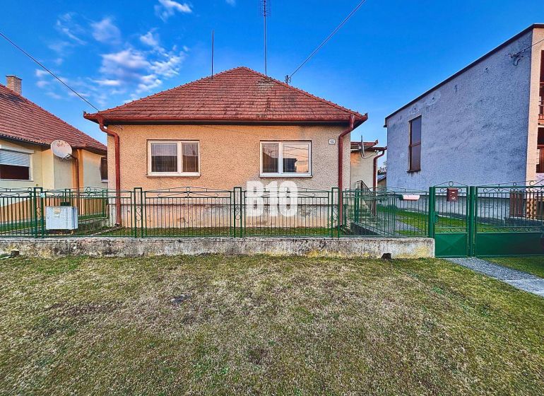 Rodinný dom s rovinatým 10a pozemkom - Rodinný dom v Sľažanoch s predzáhradkou a šikmou strechou medzi susednými budovami.