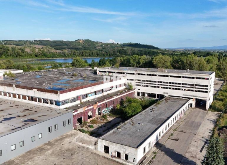 Veľkometrážne VÝROBNÉ HALY v priemyselnej zóne Géňa - Levice - Výrobné priestory v Leviciach s opustenými budovami obklopené prírodou a vodnou plochou.