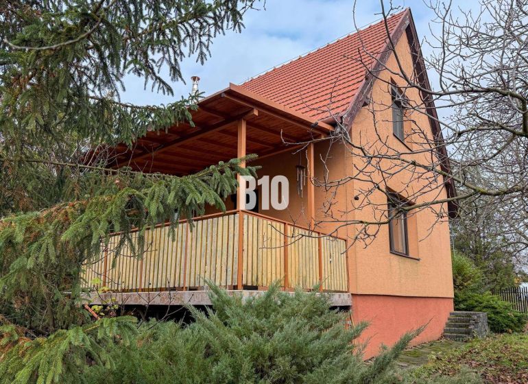 Priestranný rodinný dom s garážou na veľkom pozemku v obci Vlkas - Rodinný dom vo Vlkase obklopený zeleňou, tradične šikmá strecha, drevený balkón.