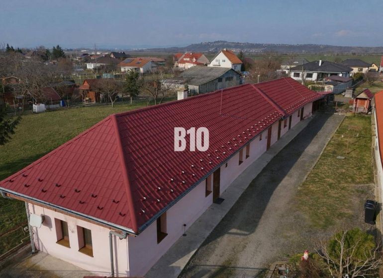 Rodinný dom s dvoma samostatnými bytovými jednotkami – Starý Hrádok - Rodinný dom v Leviciach s dlhým červeným strešným plášťom, obklopený záhradami.