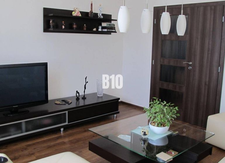 Priestranný 4 izbový byt - Solinky - Obývačka s televízorom, poličkami, stolíkom a podlahou s dreveným dekorom v 4-izbovom byte.