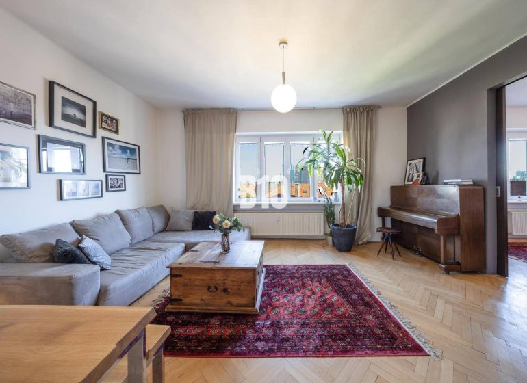 Prenájom | 2-izbový byt | Záhradnícka – Poľská ulica | 900 € + 200 € e - Obývačka s rohovou sedačkou, kobercom, klavírom a podlahou s dreveným dekorom.