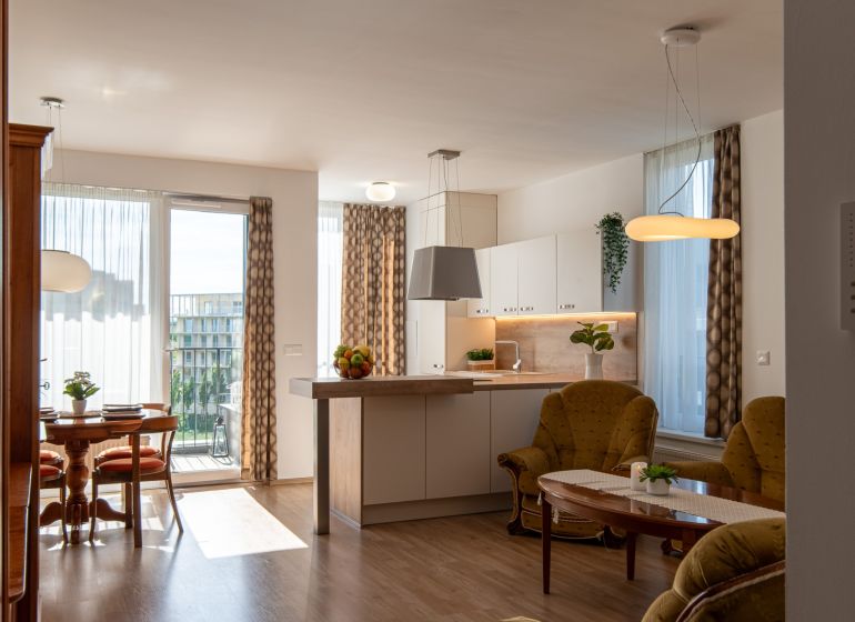 Moderný 2-izbový apartmán s parkovaním, Vila Leonardo, Bajkalská - Obývačka v 2-izbovom byte s podlahou s dreveným dekorom a svetlou kuchyňou.