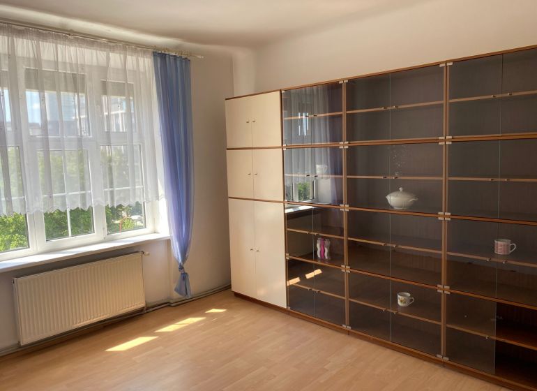 Byt na rekonštrukciu v centre Bratislavy – výborný projekt - Obývačka v 2-izbovom byte s oknom, závesmi a skriňou na policiach.
