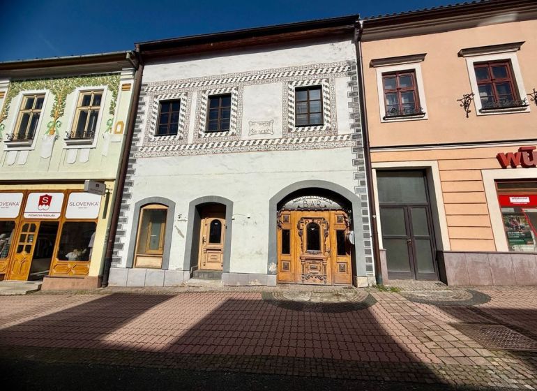 Meštiansky dom v centre Banskej Bystrice a parkovaním pre 24 áut D135Z - Ulica Dolná v Banskej Bystrici zobrazuje historické budovy s obchodmi a barom.