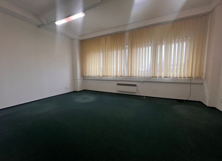 Na prenájom kancelária 24m2 - Banská Bystrica, Zvolenská cesta NO556ZL - Prázdna kancelária s tmavým kobercom a veľkými oknami so žalúziami.