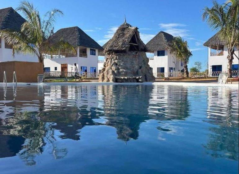 Dom pri pláži s vlastnou studňou a bazénom - Zanzibar, Uroa O578ZL - Rodinný dom v Zanzibare obklopený palmami pri bazéne pod modrou oblohou.