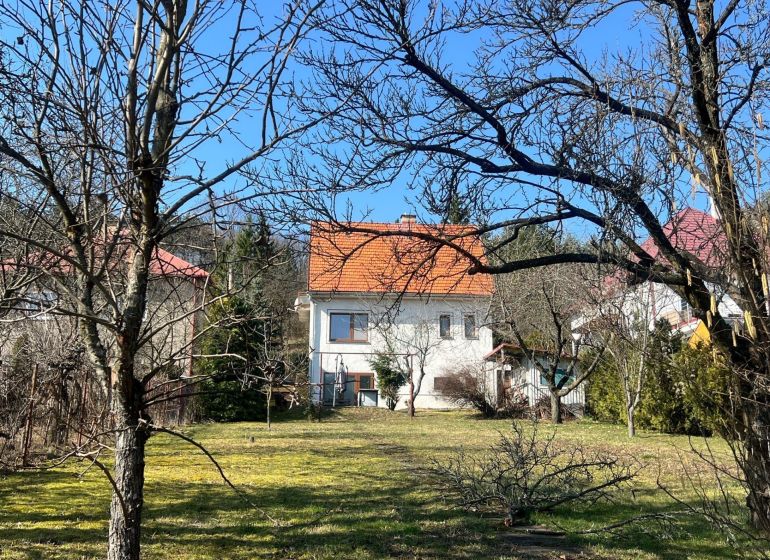 ROVINATÝ POZEMOK  S PRÍSTUPOM Z DVOCH STRÁN+ RODINNÝ DOM – B. Bystrica - Rodinný dom v Podháji, Kráľovej, obklopený stromami a trávnikom, s oranžovou strechou.