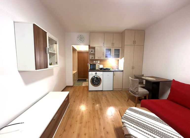 ☎️ 0918/197 701 Na prenájom garsónka s balkónom aj s výťahom   v centr - Rekreačný apartmán so vstavanou kuchyňou, červenou sedačkou a podlahou s dreveným dekorom.