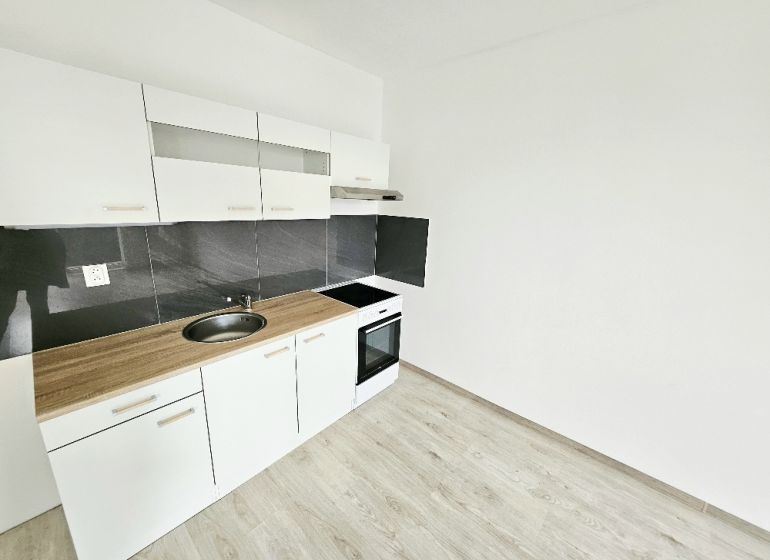 PRENÁJOM 1 IZBOVÝ BYT /34 M2/ SEVER / BALKÓN/ PIVNICA - Biela kuchynská linka s čiernym obkladom v 1-izbovom byte s podlahou s dreveným dekorom.