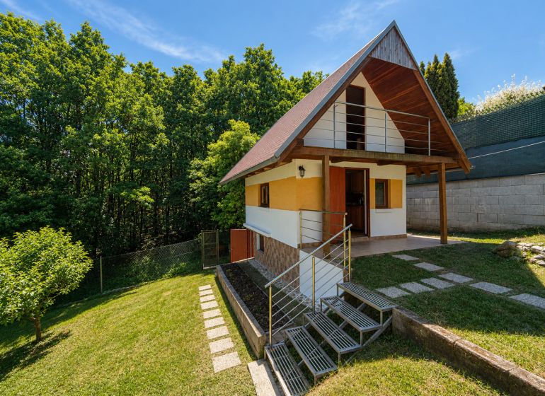 Záhrada s murovanou chatkou a výhľadom, Považská Bystrica -Klučina - Chata s dreveným dekorom v Považskej Bystrici na Klučine, obklopená zeleňou a stromami.
