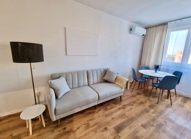 – PRENAJOM – 2 IZBOVÝ BYT – ŠALVIOVA – RUŽINOV  - Obývacia izba s pohovkou, jedálenským stolom a podlahou s dreveným dekorom v 2-izbovom byte.