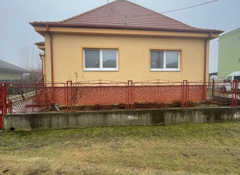 PREDAJ - 4-izbový rodinný dom s garážou, tichá lokalita, Svätoplukovo - Rodinný dom v Svätoplukove s červenou strechou, žltou fasádou a dvojicou okien.