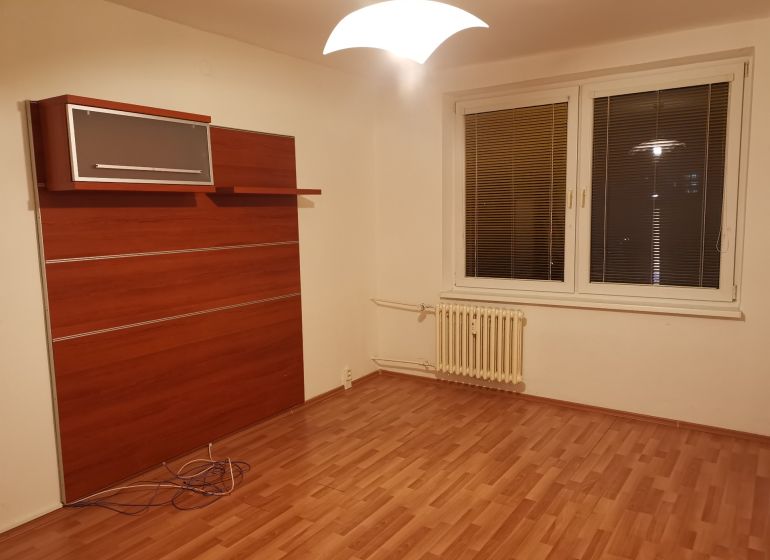 REZERVOVANÉ - Izba s podlahou s dreveným dekorom, bielymi stenami a nástennou skriňou v 3-izbovom byte.
