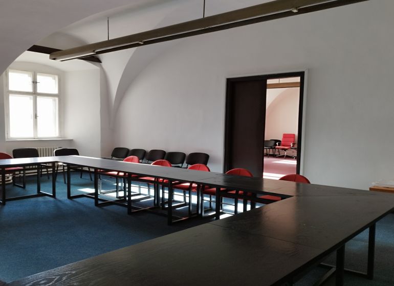 PRENÁJOM: Kancelárie 2x 50m2, Kapitulská ul.Banská Bystrica - Žena v kancelárii s plochým stolom, stoličkami a oblúkovou architektúrou v Banskej Bystrici.