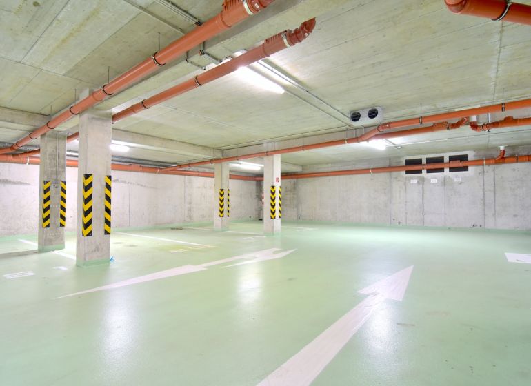 UZBECKÁ, parkovacie miesto v garáži, novostavba Oppidum - Parkovacie miesta s betónovými stenami, rúrkami a bezpečnostnými značkami v Garážach.