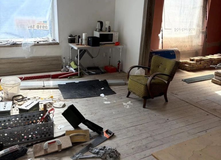 INVESTIČNÁ PRÍLEŽITOSŤ– centrum mesta | podnikanie, bývanie - Interiér s rozloženými nástrojmi, kreslom a stolom v rodinnom dome s drevenou podlahou.