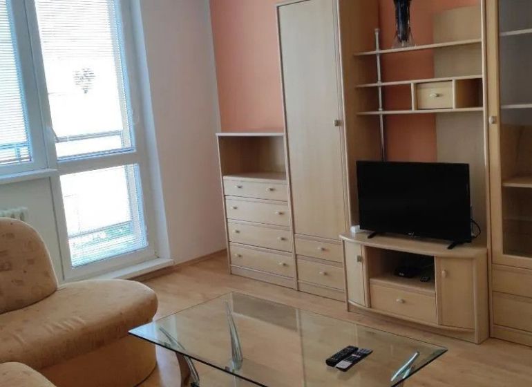 Prenájom 2 izbový byt Poprad - loggia - Obývacia izba v 2-izbovom byte s nábytkom a televízorom, podlaha s dreveným dekorom.