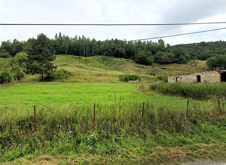 Na predaj stavebné pozemky - 7 500 m² v obci Zubné. - Zvláštne nehnuteľnosti v Zubnom: rozpadnutá stavba, tráva, stromy a kopec v pozadí.