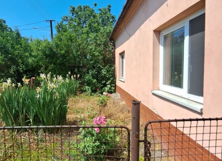 Pokojné bývanie v obci Kava + investícia do budúcnosti - Rodinný dom v Komárne s udržiavanou záhradou a plotom, jasná obloha.