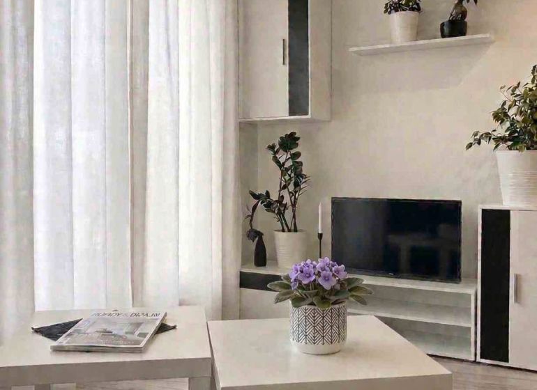 Predaj 1,5 izbového bytu s predzáhradkou, OPPIDIUM - Obývacia izba v 2-izbovom byte s bielym nábytkom a rastlinami, podlaha s dreveným dekorom.