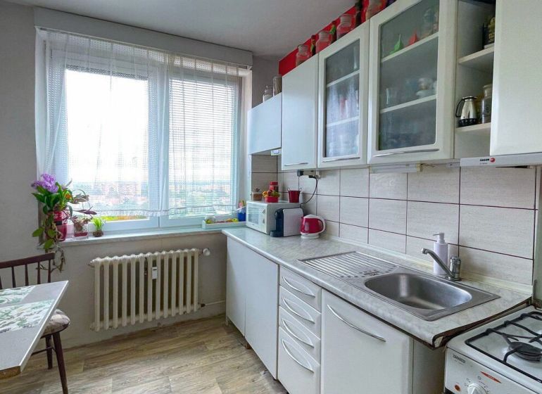 Predaj: Priestranný 3-izbový Byt s Balkónom a Potenciálom na Východe! - Kuchyňa v 3-izbovom byte s bielymi skrinkami a podlahou s dreveným dekorom.