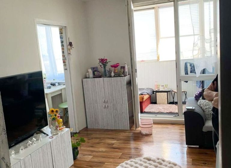 Predaj 3-izbový byt s loggiou a šatníkom – Kyjevská ul., Michalovce - Obývačka v 3-izbovom byte s podlahou s dreveným dekorom, skrinkou a televízorom.