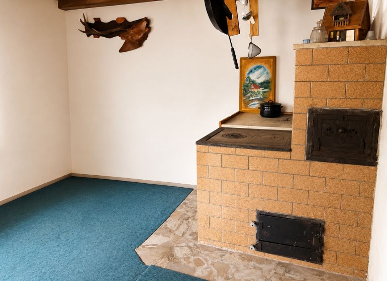 Menší Rodinný dom Veľké Košecké Podhradie, pozemok 340 m2 - Kachľová pec v rohu rodinného domu s keramickou dlažbou a obrazom na stene.