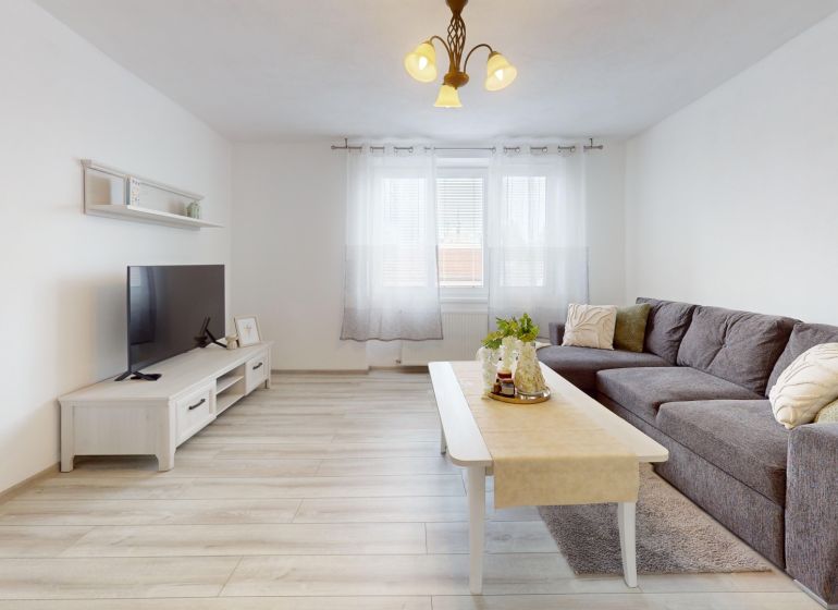  PRENÁJOM 2-izbový byt, centrum mesta s vlastným parkovaním, Topoľčany - Obývačka v 2-izbovom byte so sedačkou, TV a podlahou s dreveným dekorom.