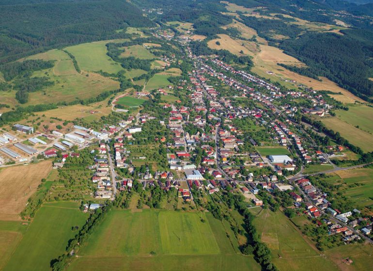 Predaj pozemkov v Badíne (podiely), okres Banská Bystrica  - Letecký pohľad na poľnohospodárske a lesné pozemky v okolí Badína, obklopené domami a budovami.