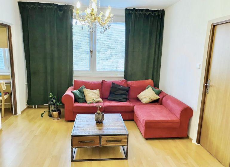 Prenajom 2,5-izbový byt v Karlovej Vsi – 48 m², výhľad do Líščieho - Obývacia izba v 2-izbovom byte s červenou pohovkou, stolíkom a závesmi.