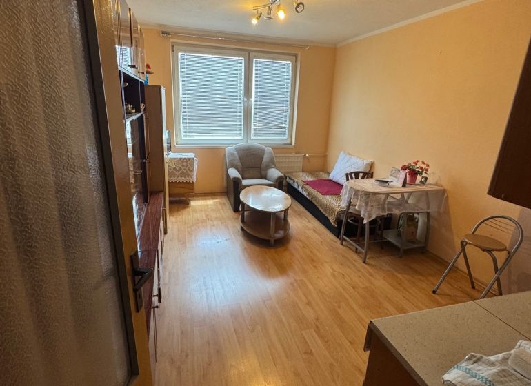 Na predaj Garsônka, 24,5 m2, s perfektnou polohou.  - Garsónka s podlahou s dreveným dekorom, jedálenským stolom a kreslami.