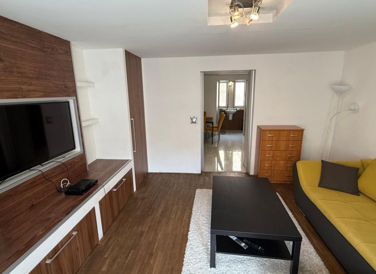 1 izbový 30m2 slnečný byt Zvolen centrum na PRENÁJOM ul. Študentská - Obývacia izba v 1-izbovom byte so sedačkou, TV a podlahou s dreveným dekorom.