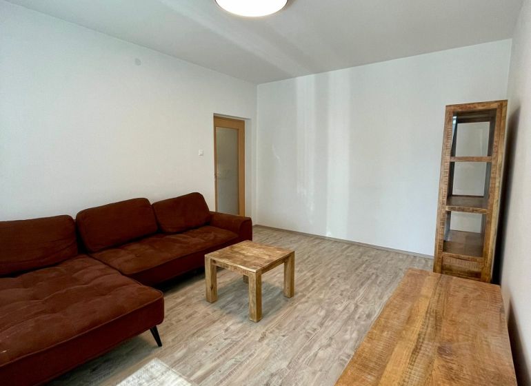 PRENÁJOM - 3-izbový byt priamo v centre Nitry s parkovaním a balkónom - Obývačka v 3-izbovom byte s hnedou sedačkou a podlahou s dreveným dekorom.