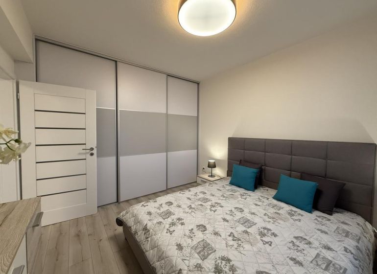 Nové skolaudované byty a apartmány vo Vajnoroch. - Spálňa v 2-izbovom byte s posteľou, šatníkovou skriňou a podlahou s dreveným dekorom.