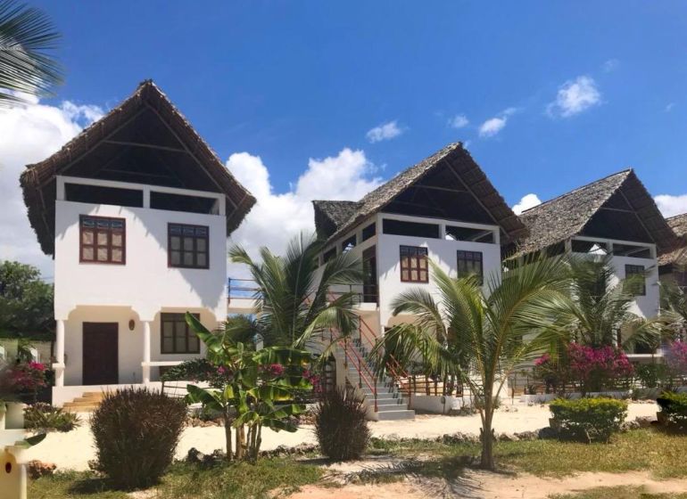 SAMOSTATNE STOJACA VILA MAPUMZIKO S 2 IZBAMI NA ZANZIBARE  - Rodinný dom v Fumba Town s palmovými stromami a trstinovou strechou pod modrou oblohou.