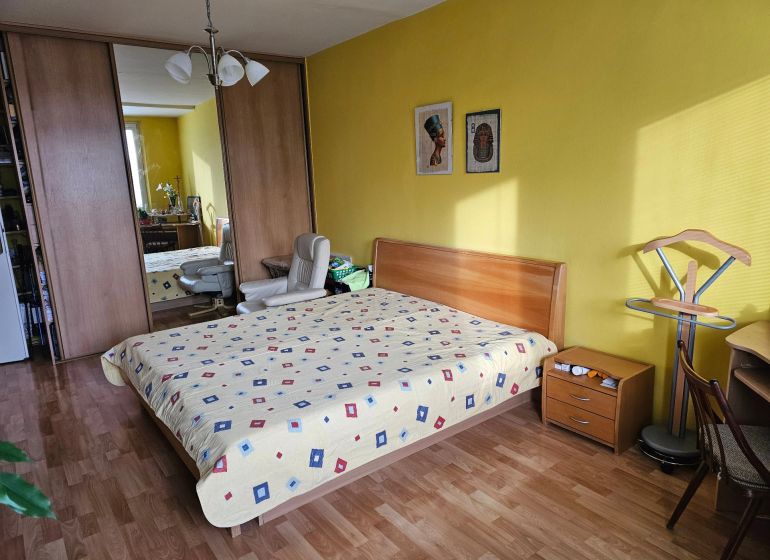 Veľký 2-izb. byt na ul. Nezábudková, Ružinov pri OC Retro - Spálňa v 2-izbovom byte s podlahou s dreveným dekorom, žltými stenami a vstavanou skriňou.