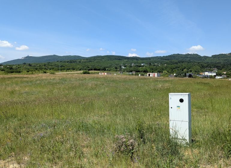 Stavebný pozemok 681 m2 v Štitároch  - Rozľahlé zelené pole s viditeľnou budovou a kopcami v Štitároch na Zamoyského, Pozemky - bývanie.