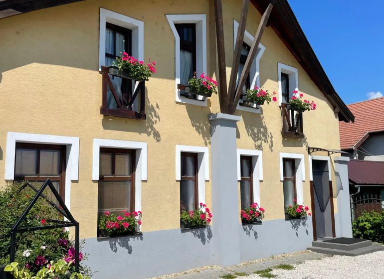 I Dom s wellness, bazénom a hotovým biznis potenciálom - Žltý rodinný dom v Hrubom Šúre so zeleným plotom a kvetinovými oknami.