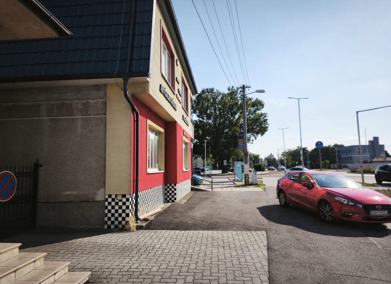 Prenájom obchodno-administratívneho priestoru , Šaľa  centrum - Obchodné priestory na ulici SNP v Šali s červeným autom na ceste.