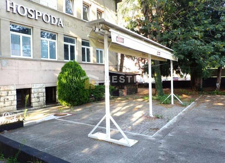 Reštaurácia s terasou na prenájom – centrum mesta - Obchodné priestory v Senici s parkoviskom, zeleňou a nápisom na budove.