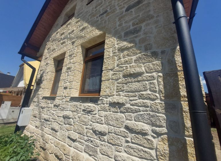 NA PREDAJ Čarovný vidiecky dom s kachľovou pecou NEMECKÁ - Kamenná fasáda rodinného domu v Nemeckej s dreveným dekorom na streche.