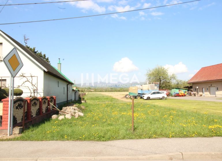 NA PREDAJ: Stavebný pozemok pri hlavnej ceste – Sačurov - Pozemky - bývanie v Sačurove s domami, trávnikom a cestnou značkou.